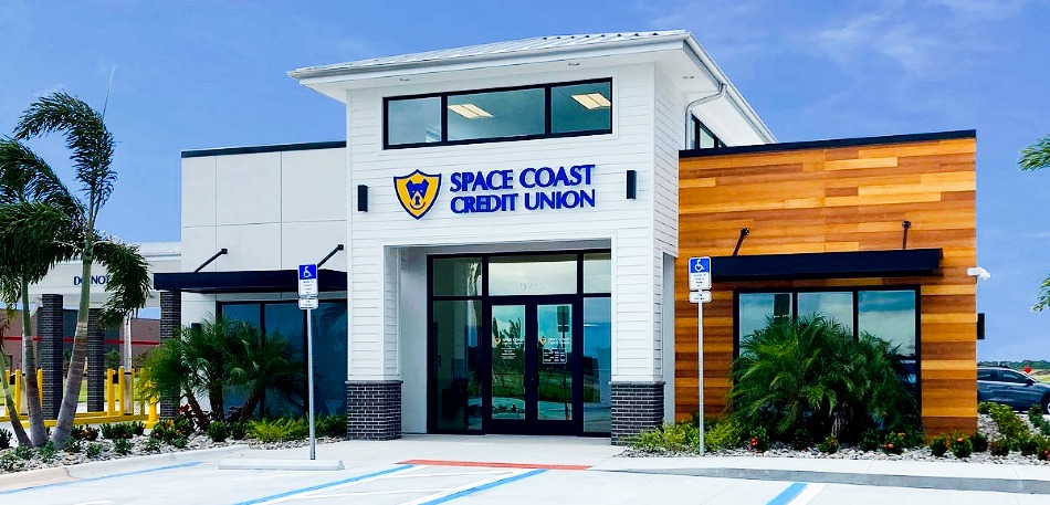 Exterior view of a Space Coast Credit Union branch building with modern design, palm trees, and clear blue sky.